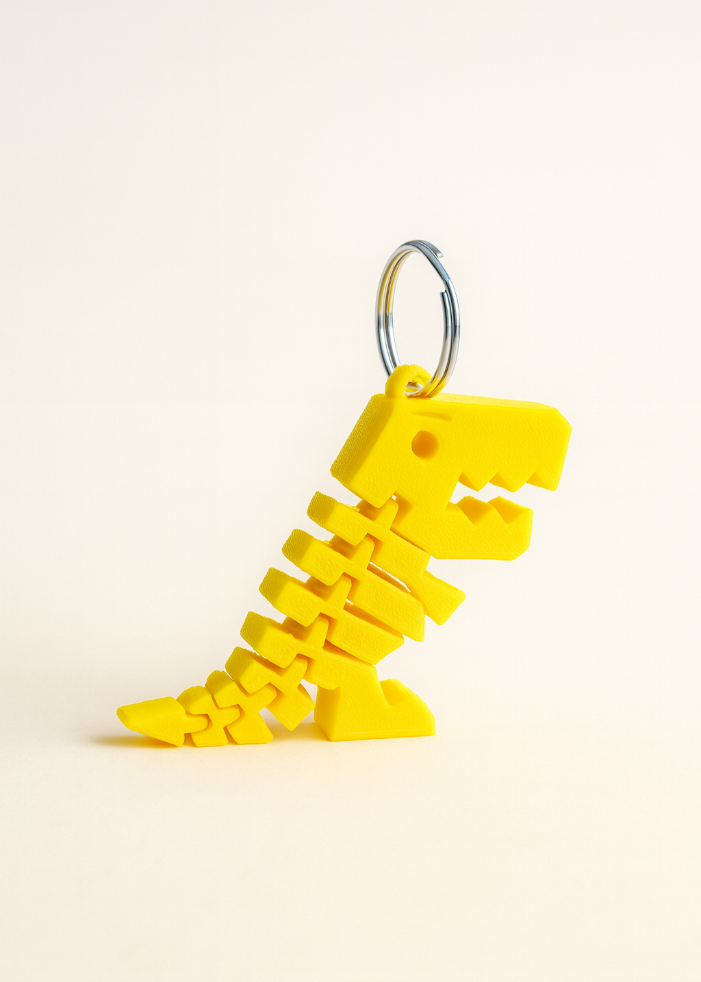 3D-printed articulated T-Rex dinosaur keychains in yellow and red on a wooden surface
